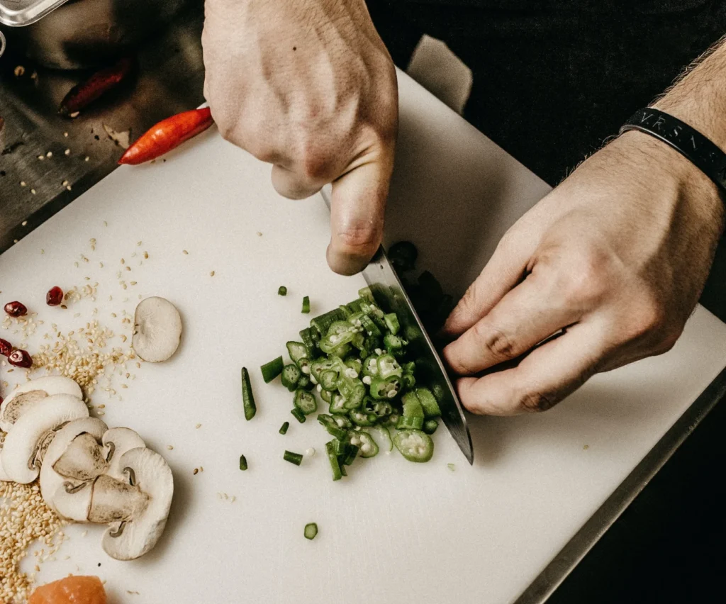 Händer som ses hålla i kniv och hacka upp grön chilifrukt